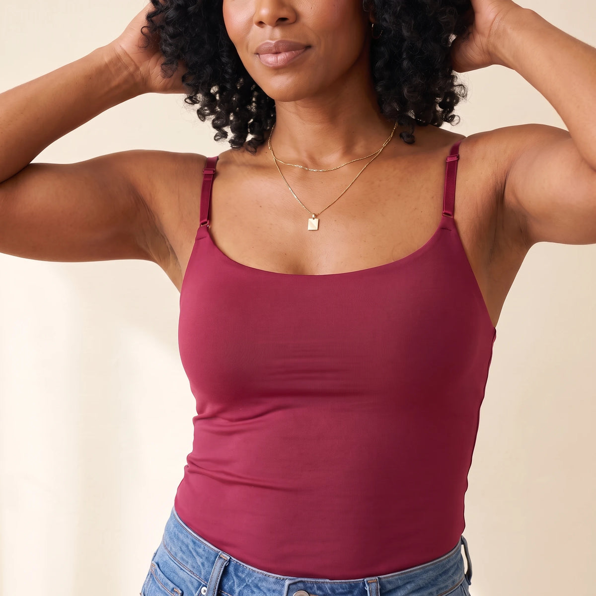 Close-up of the Cerise burgundy Kischt Aurelle cami with arms raised, showing the scoop neckline, thin straps and a smooth seamless front with the built-in bra hidden inside
