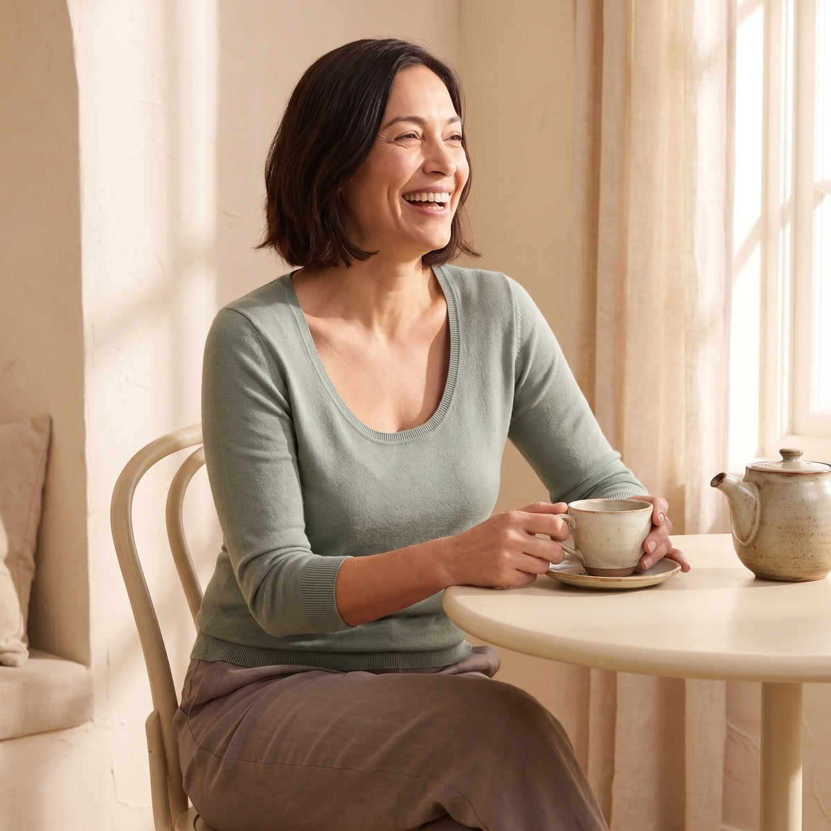 Laughing woman in her forties at a café table in a sage scoop-neck top over the Blanc white Kischt Camille balconette bra