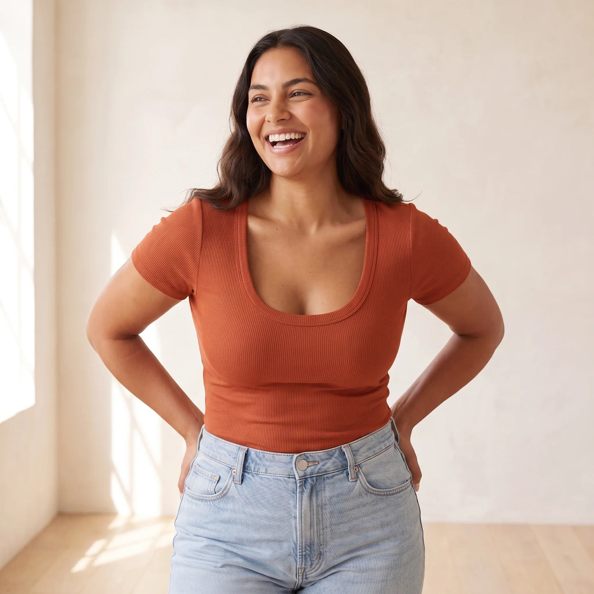 Laughing woman in a rust scoop-neck T-shirt and jeans wearing the Cerise red Kischt Camille balconette bra underneath