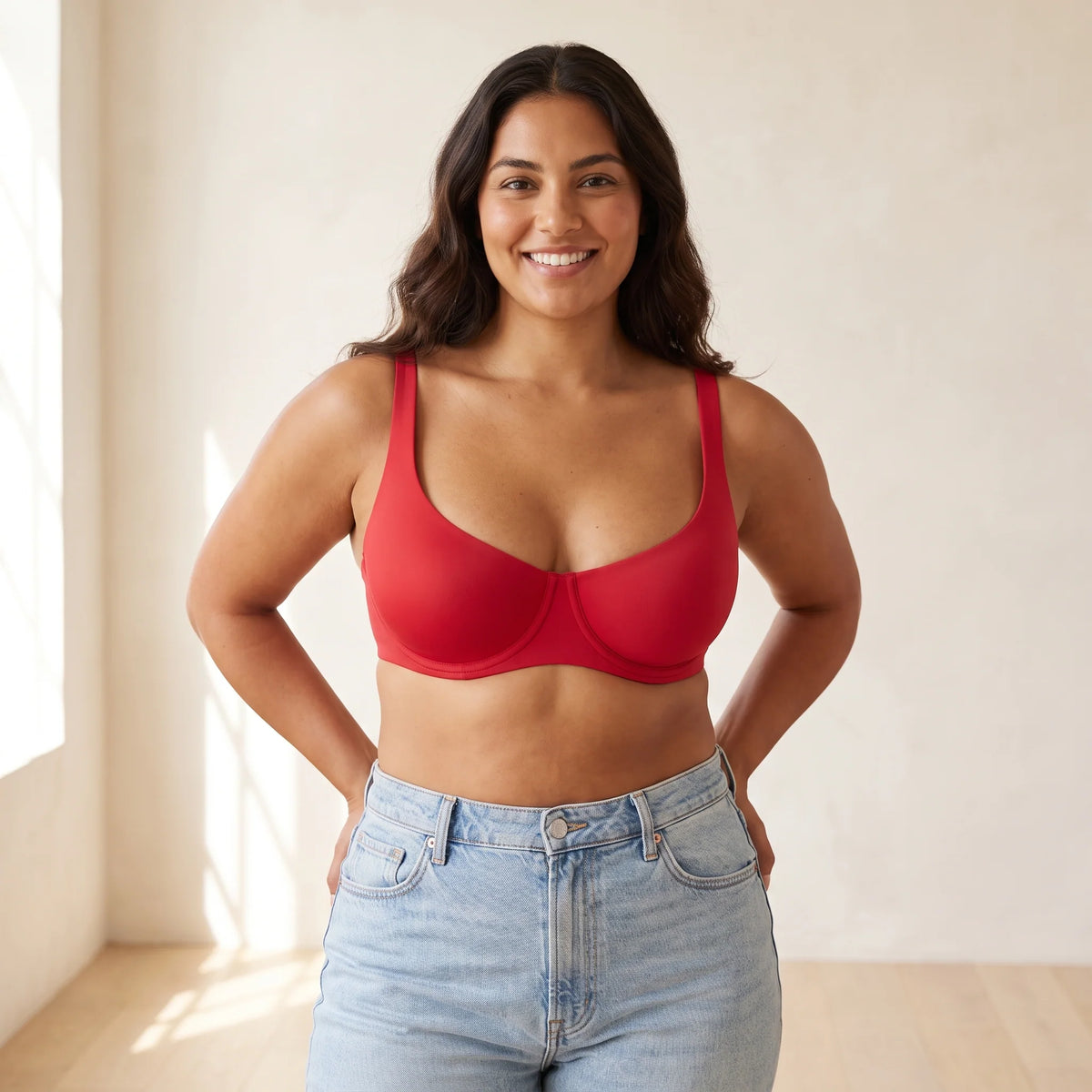 Woman with long dark hair, hands on hips, wearing the Kischt Camille unlined balconette underwire bra in Cerise red with jeans
