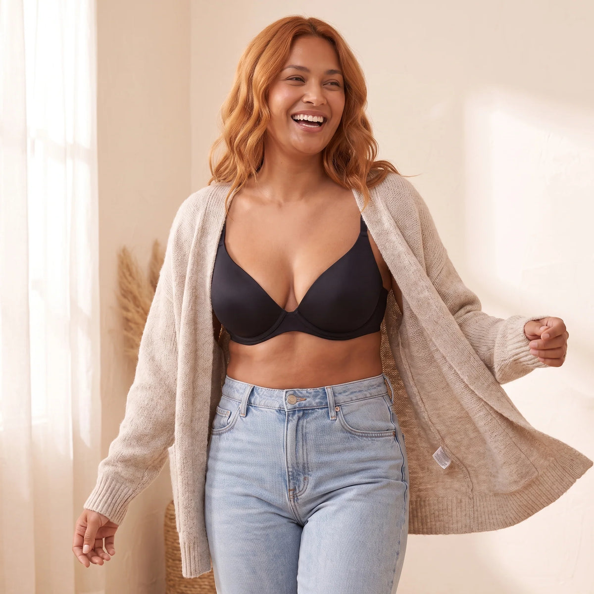 Laughing woman walking in an open oatmeal cardigan and jeans, wearing the Noir black Kischt Juliette plunge bra underneath