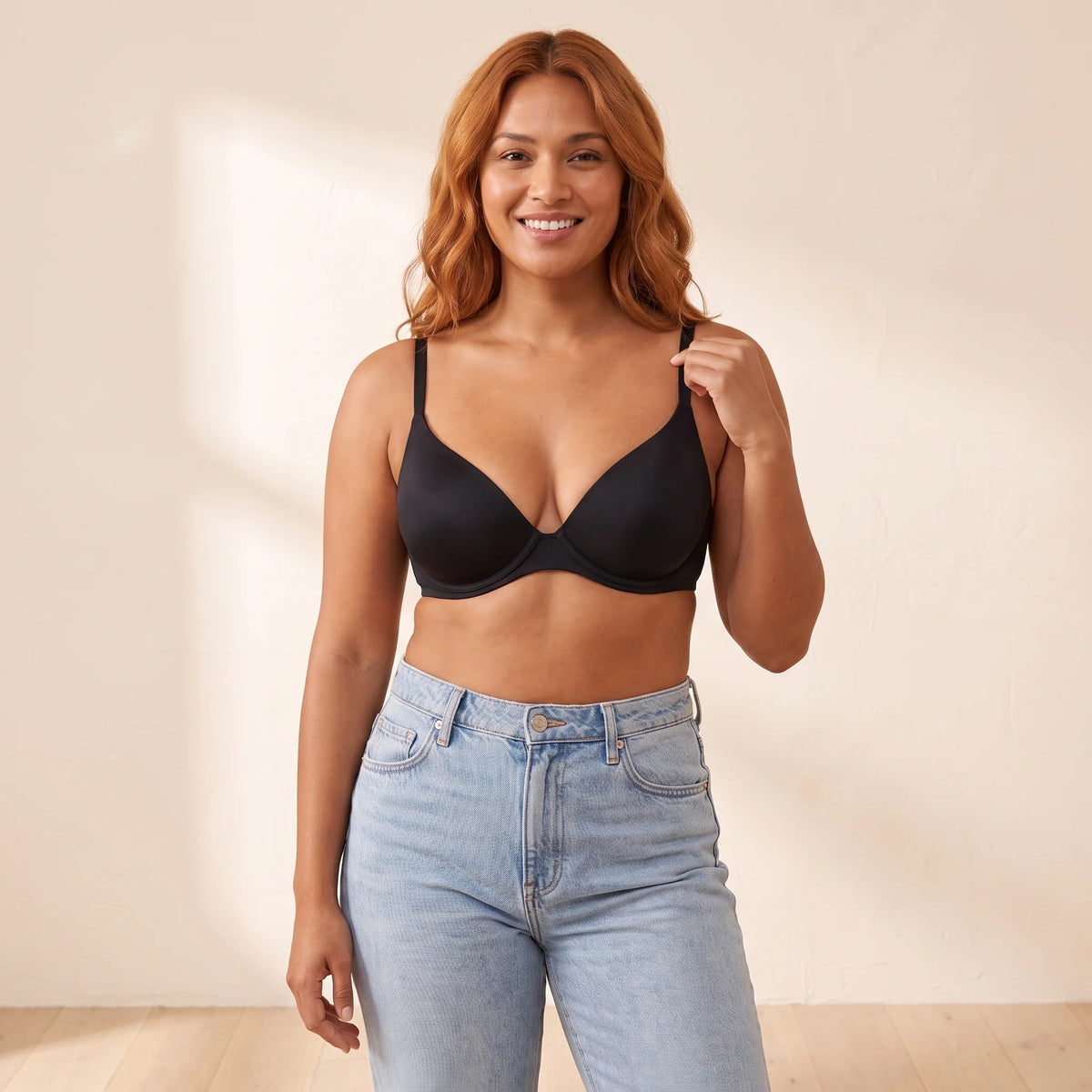 Smiling woman with copper hair wearing the Kischt Juliette unlined plunge underwire bra in Noir black with light-wash jeans