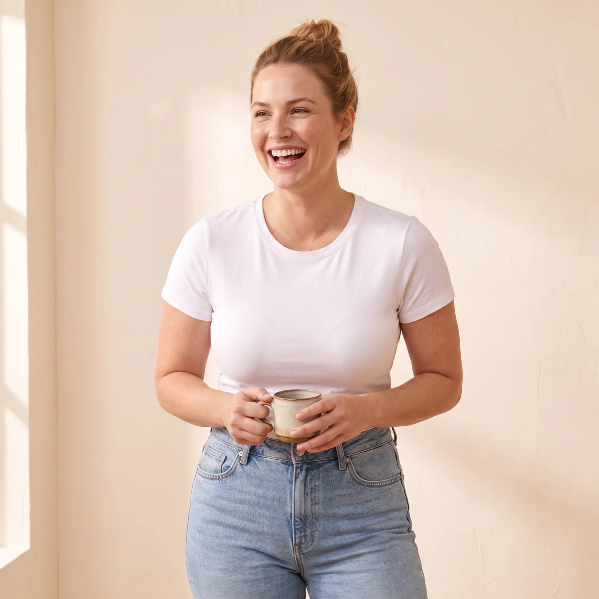 Woman in a white T-shirt and jeans wearing the Crème nude Kischt Léonie sports bra underneath for a smooth, lifted shape