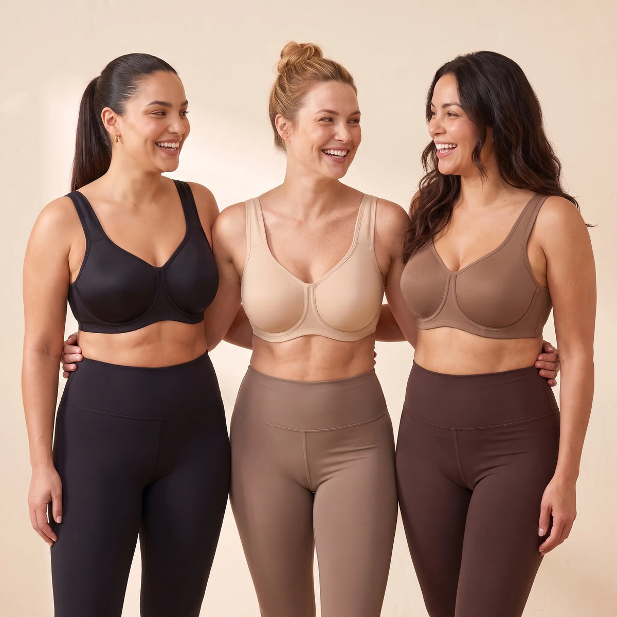 Three women with fuller busts wearing Kischt Léonie underwire sports bras in Noir black, Crème nude and Mocha brown