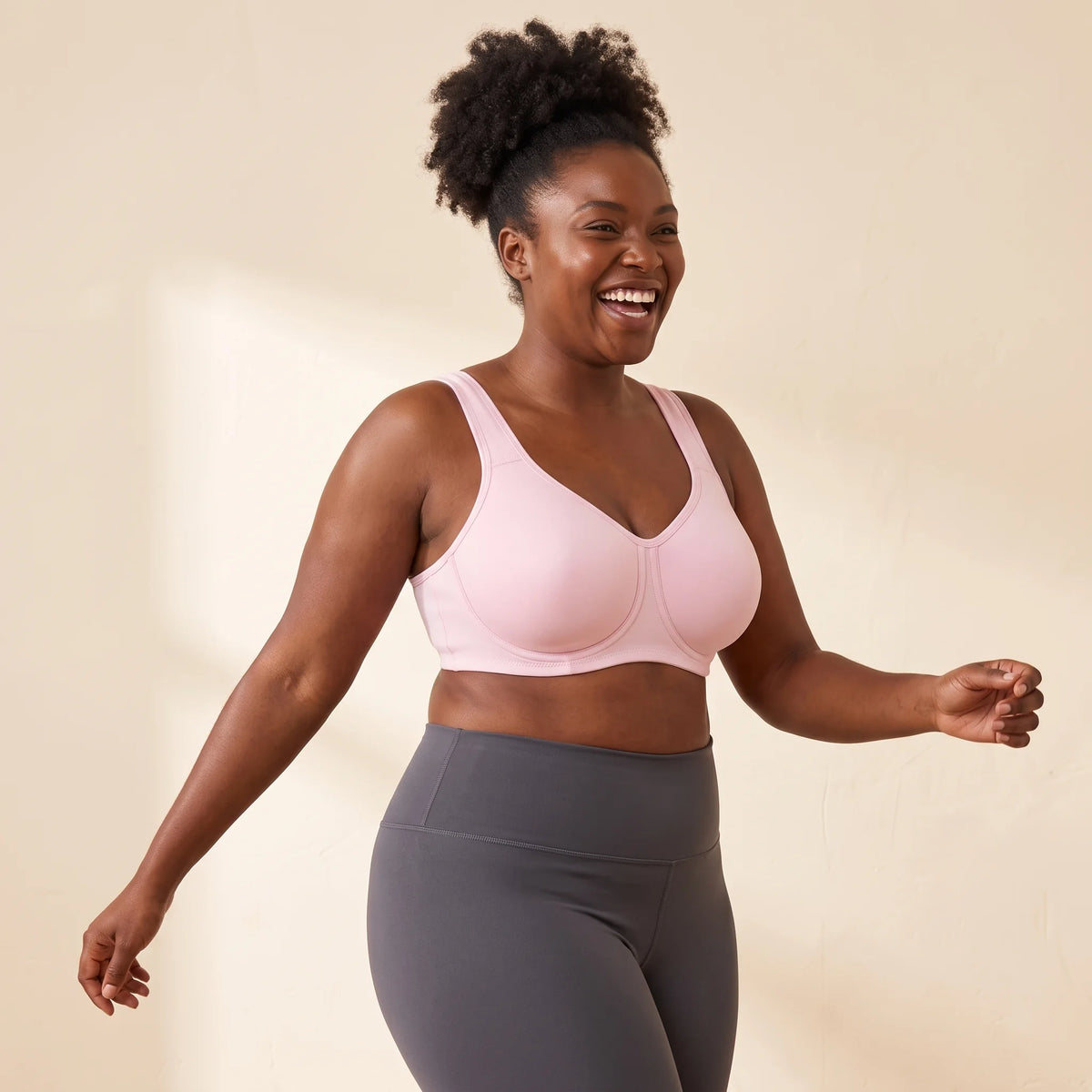 Laughing woman with a full bust warming up in the Kischt Léonie high impact underwire sports bra in Blush pink with charcoal leggings
