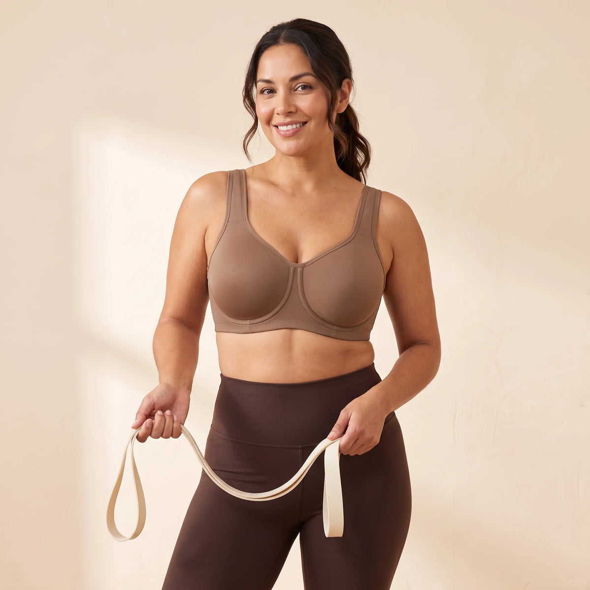 Woman with a full bust warming up with a resistance band in the Kischt Léonie high impact underwire sports bra in Mocha brown