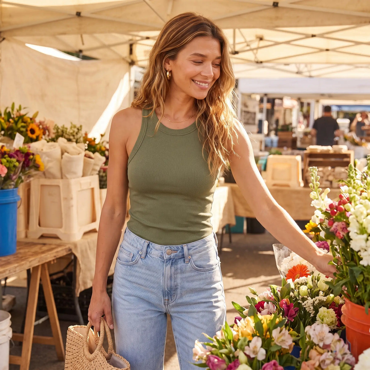Woman at a sunny market in the Olive army green Kischt Noemi ribbed racerback tank top with built-in bra, jeans and a straw bag
