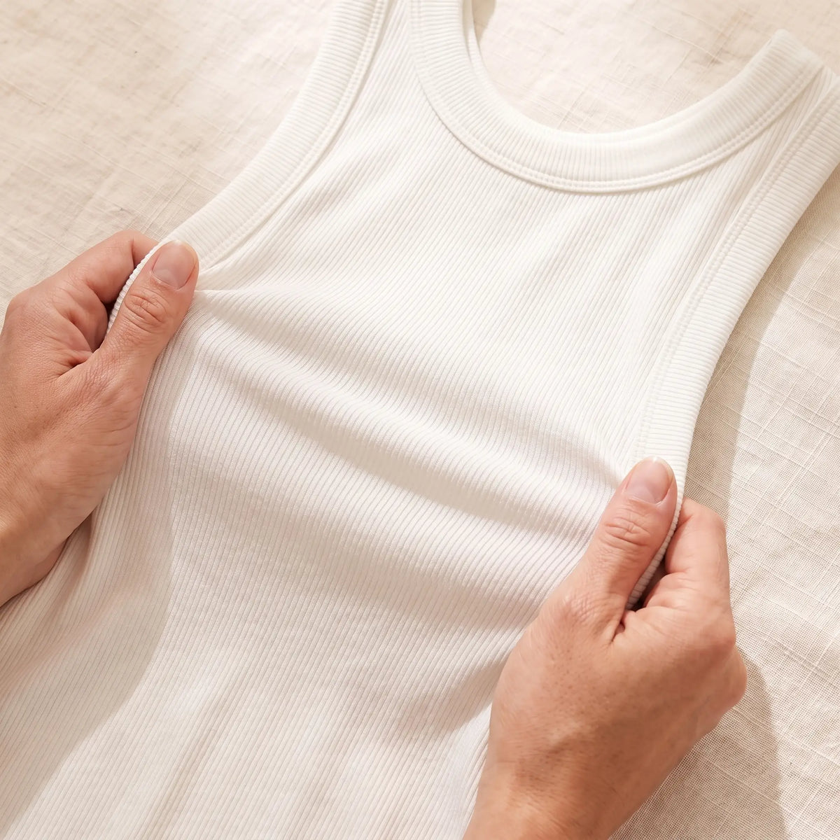 Hands stretching the soft rib knit of the Blanc white Kischt Solene tank top